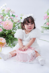 Child with Cake and Floral Decor: An adorable child, dressed in a white dress, sits with a pink cake in a room adorned with delicate floral decorations.
