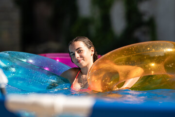Teenager girl relaxing in swimming pool with colorful inflatable rings