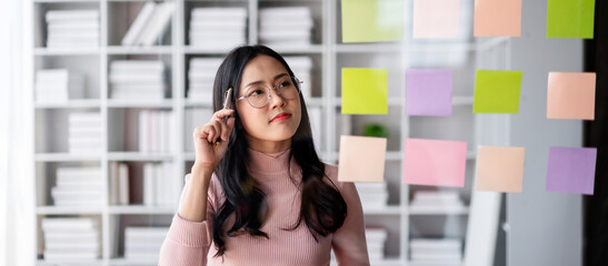 Asian Woman Thinks at Office with Colorful Notes on Glass Wall Idea Generation Business Brainstorming and Planning Strategy for Project