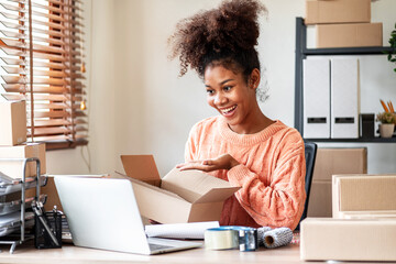 African American Young Woman Opens Cardboard Box Package with Laptop for Online Business or E-Commerce at Home Office for Delivery and Shipment