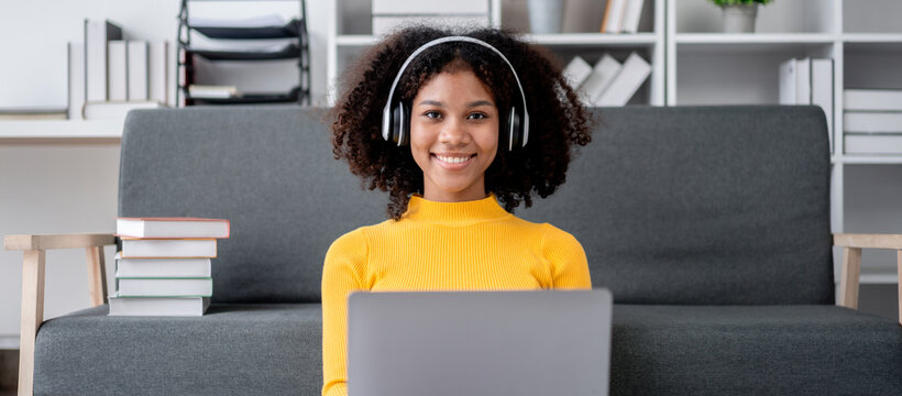 Young Women Smiling Using Laptop on Sofa at Home Studying or Working and Listen to Music via Headphones E-learning or Online Courses