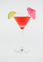 A red cocktail in a classic martini glass with a wedge of lime and an umbrella set against a white background.