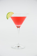 A red cocktail in a classic martini glass with a wedge of lime set against a white background with copy space to the right.