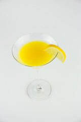 An orange cocktail in a classic martinin glass with a wedge of lemon set against a white background viewed from above. This is a macro image.