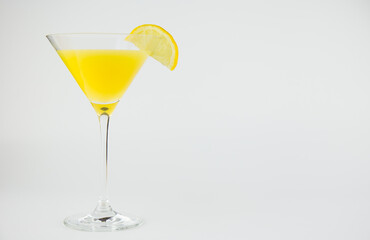 An orange cocktail in a classic martinin glass with a wedge of lemon against a white background with copy space to the right hand side.