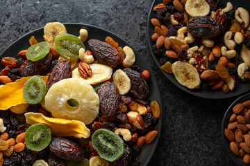 Dried tropical fruits, nuts, and raisins in black plate.