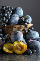 Blue grapes, blue plums, and figs on a black stone table.