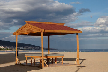 Empty gazebo with massage couch on beach against backdrop of stormy sky at beginning of season .Concept of beach holidays, summer, relaxation, self-care