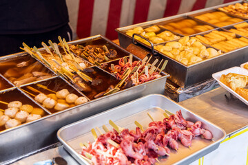 Colorful skewered seafood, tofu, vegetables and meats cook in hot broth at Japanese (oden) stand, highlighting the variety of local street cuisine