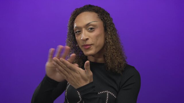 Transgender hispanic woman makes money gesture with fingers in a purple studio set; greed wealth desire.