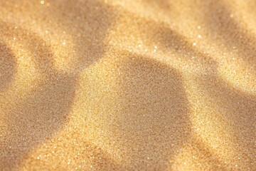 Obraz premium Close-up of fine golden sand grains with sparkling light reflections creating soft shadow patterns