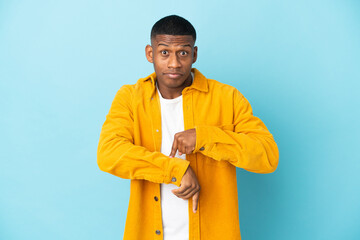 Young latin man isolated on blue background making the gesture of being late