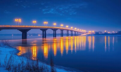 Fototapeta premium Long illuminated bridge over calm water at dusk with glowing streetlights reflecting on the surface and snow-covered riverbank