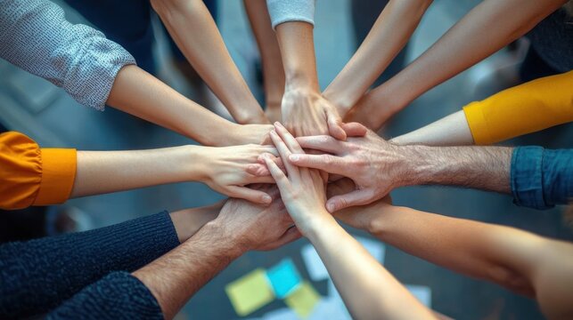 Multiple hands stacked together symbolizing unity, teamwork, and collaboration in a diverse group with casual clothing indoors - Powered by Adobe