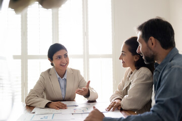 Indian female broker or agent presenting to couple clients market data, property listings, explain investment analysis results, discussing papers filled with charts during formal meeting in office