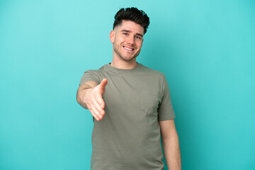 Fototapeta premium Young caucasian man isolated on blue background shaking hands for closing a good deal
