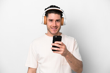 Young caucasian man isolated on white background listening music with a mobile and looking front