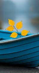 Obraz premium Yellow birch leaves on a blue boat on a calm lake in autumn season and landscape
