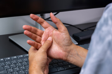 Man massaging strained palm over keyboard, indicating repetitive typing injury in a modern clinical office. Perfect for ads on work-related palm pain relief, muscle rehab, and tendon therapy.