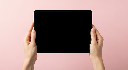 Two hands hold a black tablet computer against a pale pink background.  The screen is dark and blank, ready for content.