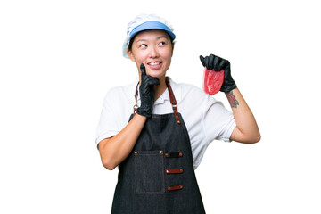 Young caucasian woman wearing an apron and serving fresh cut meat over isolated background thinking an idea while looking up