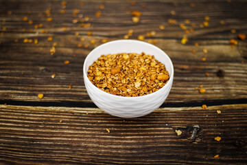 A white ceramic bowl of homemade granola on a rustic dark wood table with scattered oats for a healthy breakfast.