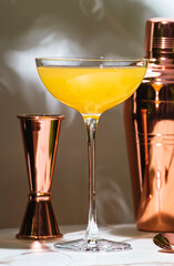 Yellow alcoholic cocktail drink with whiskey, liqueur and lemon juice with bar tools. Marble table in elegant lobby