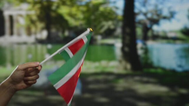 Man holding suriname flag in outdoor park setting with blurred background showing lush greenery and peaceful lake surroundings highlighting national pride and diversity.