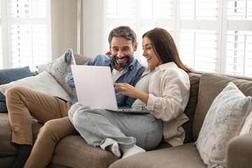 Couple in love relaxing on comfortable couch with laptop, enjoy online shopping through marketplace platform or websites, planning vacation, buying tickets, booking hotels, renting apartment remotely