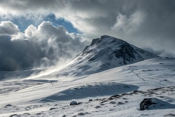 Obraz premium Dramatic snow covered mountain peak under stormy cloudy sky with sunbeams breaking through