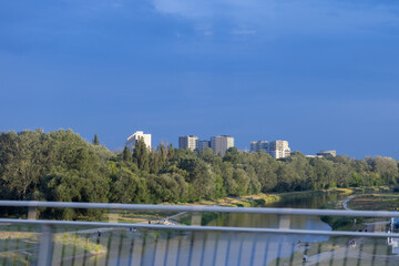 Scenic urban landscape depicts a tranquil river, dense green foliage, and sleek modern residential buildings beneath a bright blue sky, showcasing ecological balance