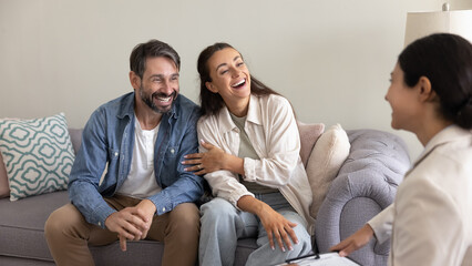 Cheerful married couple sitting on sofa at home, smiling, while engaging with pleasant, positive...
