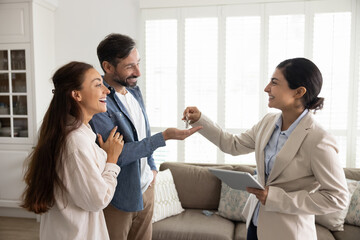 Happy Indian real-estate agent sold house to Latin couple, giving bunch of keys, congratulate with good purchase or short rent holiday flat. Tenancy, transaction of selling and buying property, travel