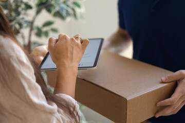 Close up cropped photo of woman holding digital tablet and signing receipt as male courier delivers package with ordered goods to her doorsteps. Comfortable, excellent delivery services, acceptance