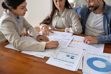 Professional female mortgage advisor sits at table with married couple, reviewing together real...