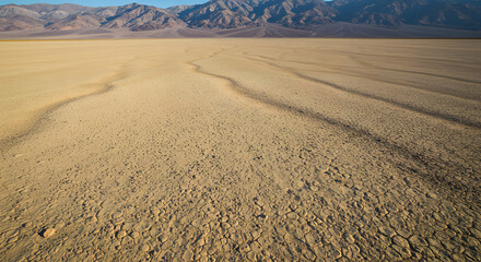Undulating patterns on a vast, dry, cracked lakebed in a desert valley with mountains in the background.