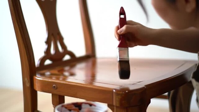 A person applies a fresh coat of varnish to a wooden chair, enhancing its appearance and preserving its for longevity.