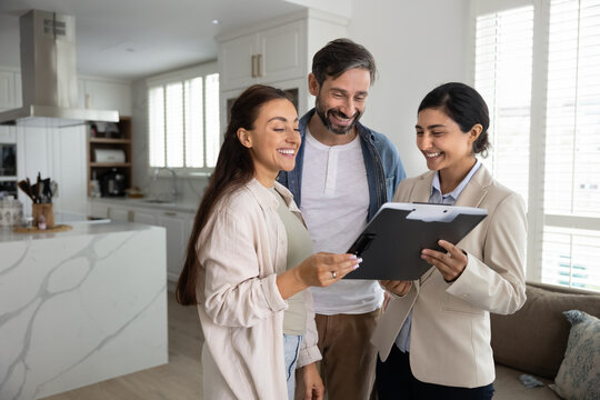 Couple reviewing mortgage or real estate documents during meeting with Indian woman agent, examining lease agreement and legal papers related to purchasing or renting property, learn insurance policy