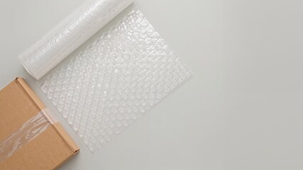 Light background with bubble wrap roll, corrugated box, and packing tape arranged flatly, room for text