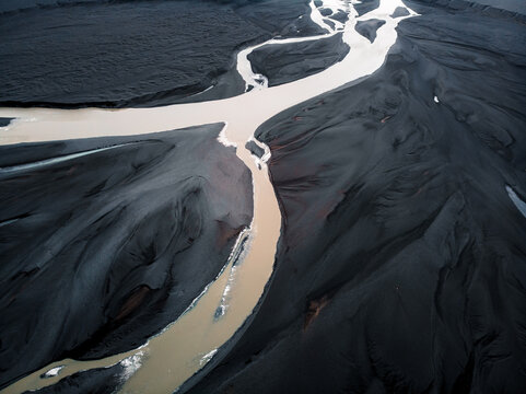 Aerial view of a braided river winding through volcanic and alluvial plains in Iceland, shaped by the forces of glacial outburst floods (j&ouml;kulhlaup). The contrasting textures and colors of water, sedi