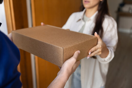 Female customer receiving parcel box from delivery man at entrance, reflecting satisfaction with express doorstep delivery services. Dependable logistics, easy dispatch, international transportation