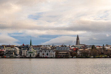 Fototapeta premium View of Reykjavík’s skyline seen from across the city lake, with buildings reflecting in the calm water. A peaceful combination of urban architecture and natural scenery.
