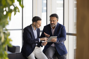 Diverse male colleagues using tablet for teamwork, analyzing online product sales growth,...