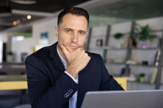 Serious confident young Latin business man posing at workplace, touching chin, looking at camera. Handsome 30s Hispanic executive, CEO, lawyer, financial director professional portrait - Powered by Adobe