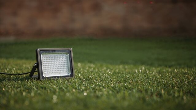 Outdoor floodlight positioned on grass with attached wire