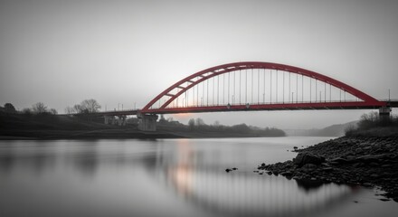 Naklejka premium Red Arch Bridge Over Calm Water Surrounded by Misty Landscape at Sunset