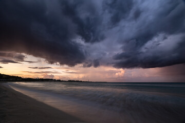 Obraz premium Dark dramatic seascape stormy clouds, distant rain and waves crashing on sandy beach, Sicily, Italy