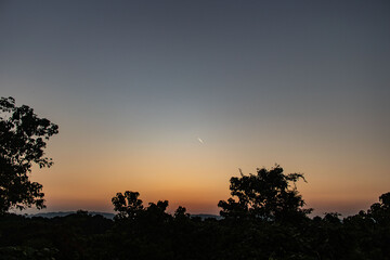 Sunlit forest hill reflecting in lake during golden hour.