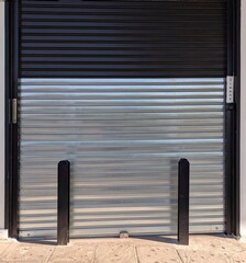 Fachada de una tienda con puerta cerrada por cortina plegable de metal, protegida con vigas de metal