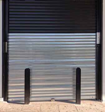 Fachada de una tienda con puerta cerrada por cortina plegable de metal, protegida con vigas de metal